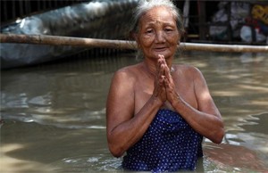 A woman standing on a flooded road prays. Photo by AP/ Khin Maung Win.