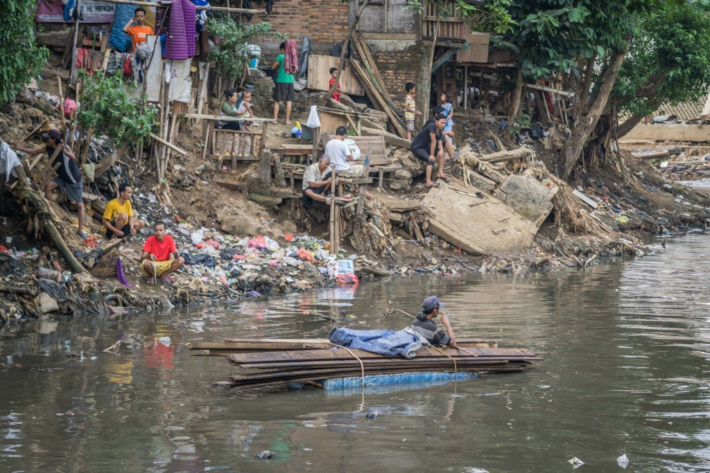 A river-based rubbish savager (pemulung) floating in the filthy river with his cigarette.