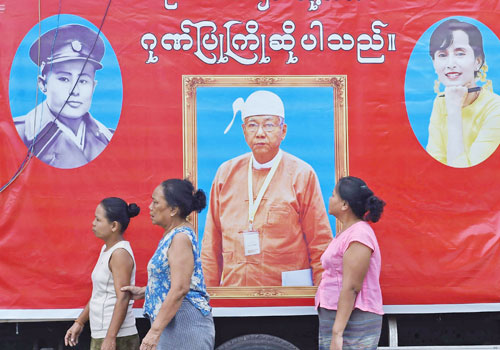 Relatives and sympathisers of political prisoners wait outside Insein Prison in Yangon on April 8 in front of a banner bearing the portraits of President U Htin Kyaw, Daw Aung San Suu Kyi and Bogyoke Aung San. Photo: AFP